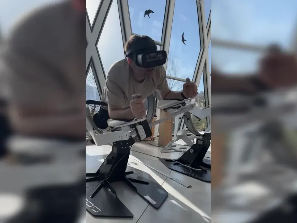 משתתף עם משקפי VR מניע את הגוף ואוחז בבקרי מתקן ICAROS.